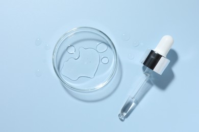 Photo of Cosmetic product in Petri dish and dropper on light blue background, top view