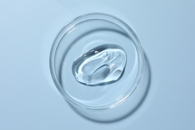 Photo of Cosmetic product in Petri dish on light blue background, top view