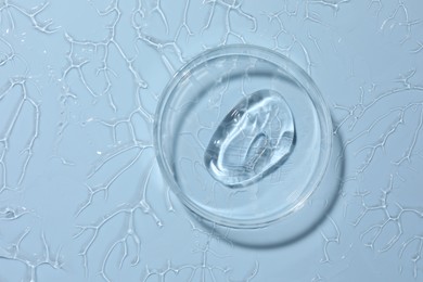 Photo of Cosmetic product in Petri dish on light blue background, top view