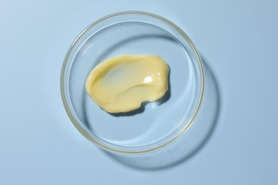 Photo of Cosmetic product in Petri dish on light blue background, top view