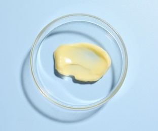 Photo of Cosmetic product in Petri dish on light blue background, top view