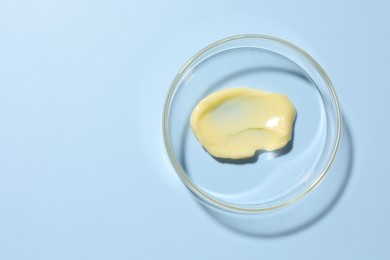 Photo of Cosmetic product in Petri dish on light blue background, top view. Space for text