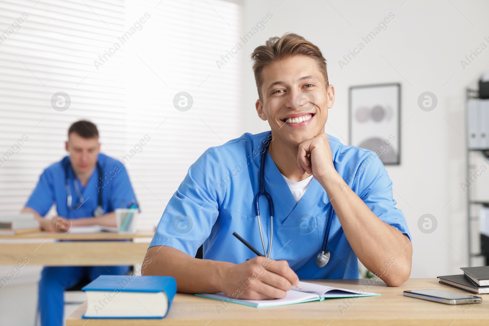 Photo of Medical students in uniforms studying at desks indoors, selective focus