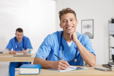 Photo of Medical students in uniforms studying at desks indoors, selective focus