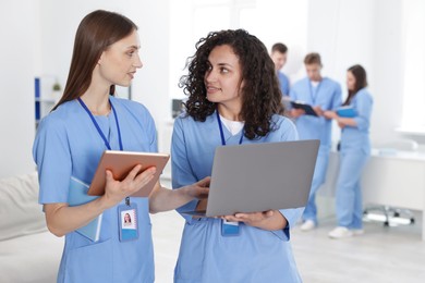 Photo of Medical students in uniforms with tablet and laptop indoors, selective focus