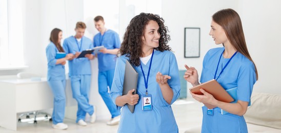 Photo of Medical students in uniforms with tablet and laptop indoors, selective focus