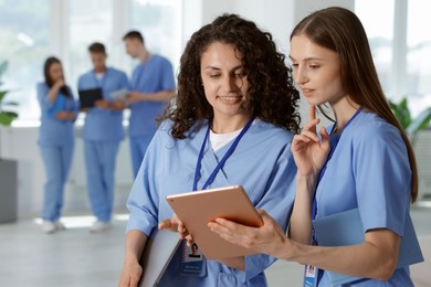 Photo of Medical students in uniforms with tablet and laptop indoors, selective focus