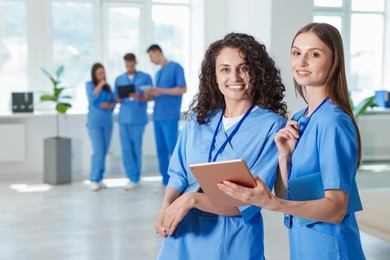 Photo of Medical students in uniforms with tablet and laptop indoors, selective focus