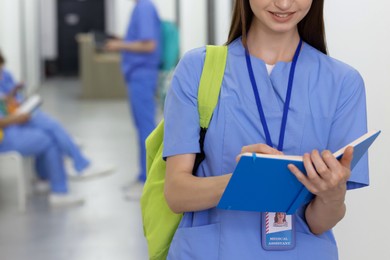 Photo of Medical student in uniform with backpack and notebook indoors, selective focus