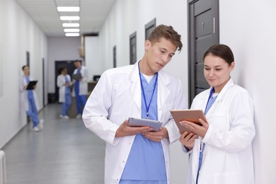 Photo of Medical students in uniforms with tablets indoors, selective focus
