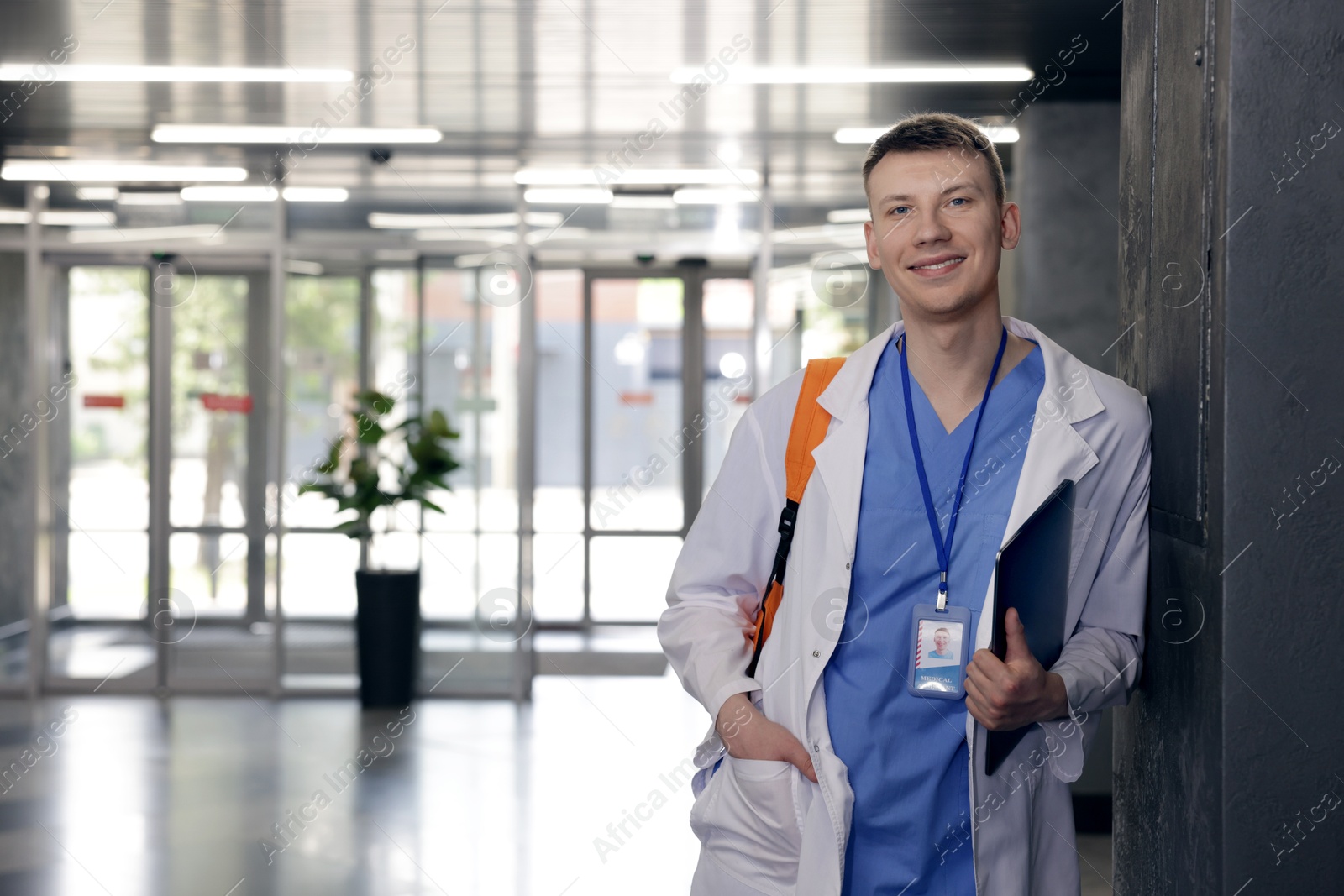 Photo of Medical student in uniform with backpack and laptop indoors, space for text