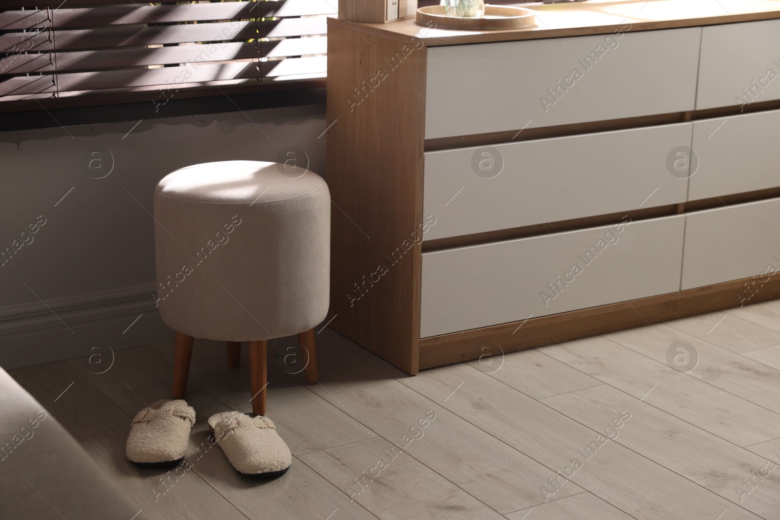 Stylish pouf and slippers near chest of drawers at home Photo of Stylish pouf and slippers near chest of drawers at home