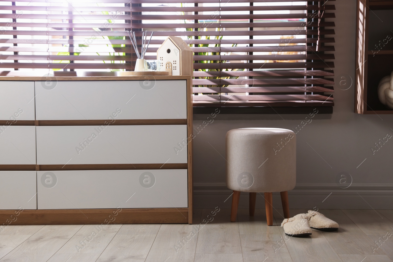 Stylish pouf and slippers near chest of drawers at home Photo of Stylish pouf and slippers near chest of drawers at home