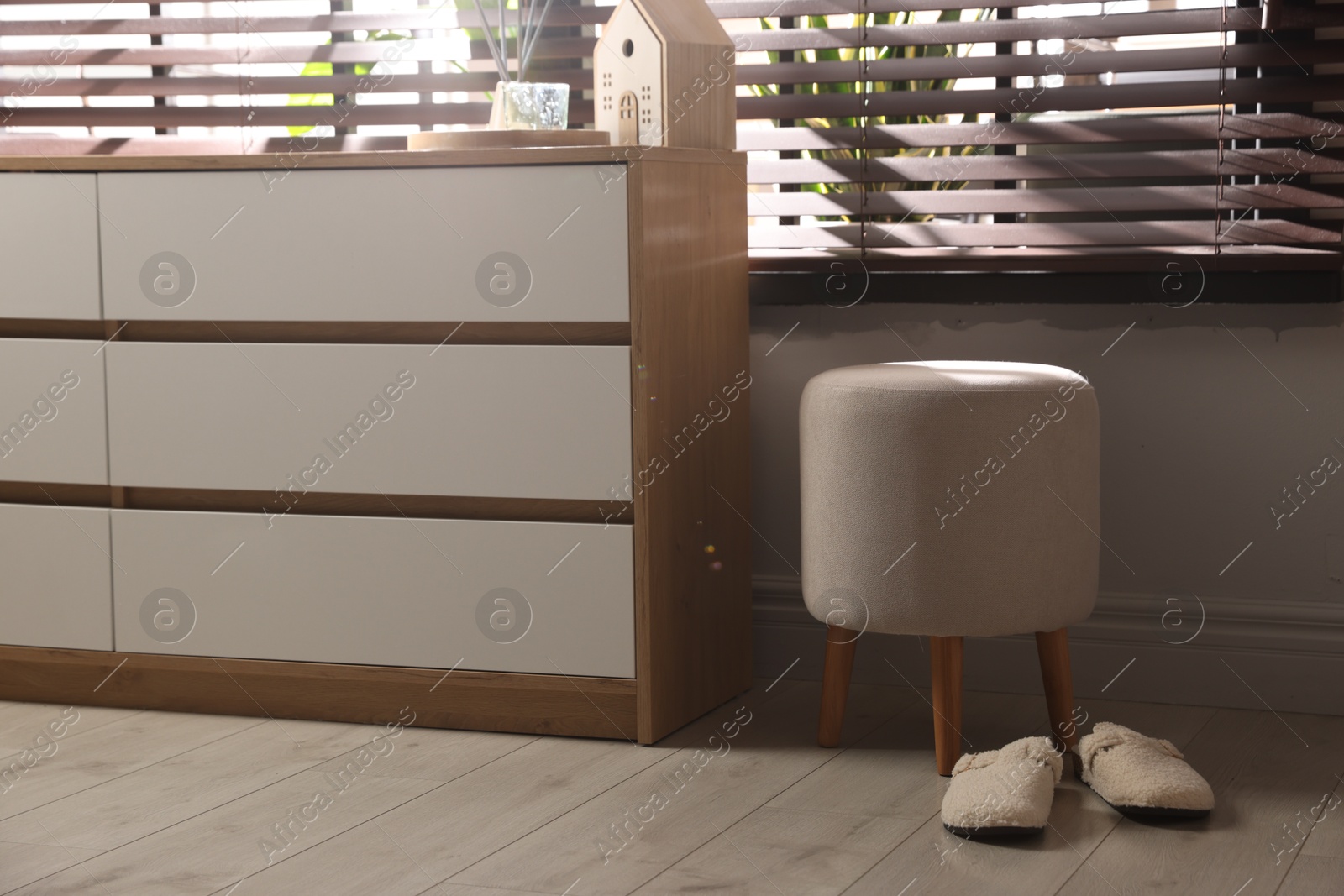 Stylish pouf and slippers near chest of drawers at home Photo of Stylish pouf and slippers near chest of drawers at home