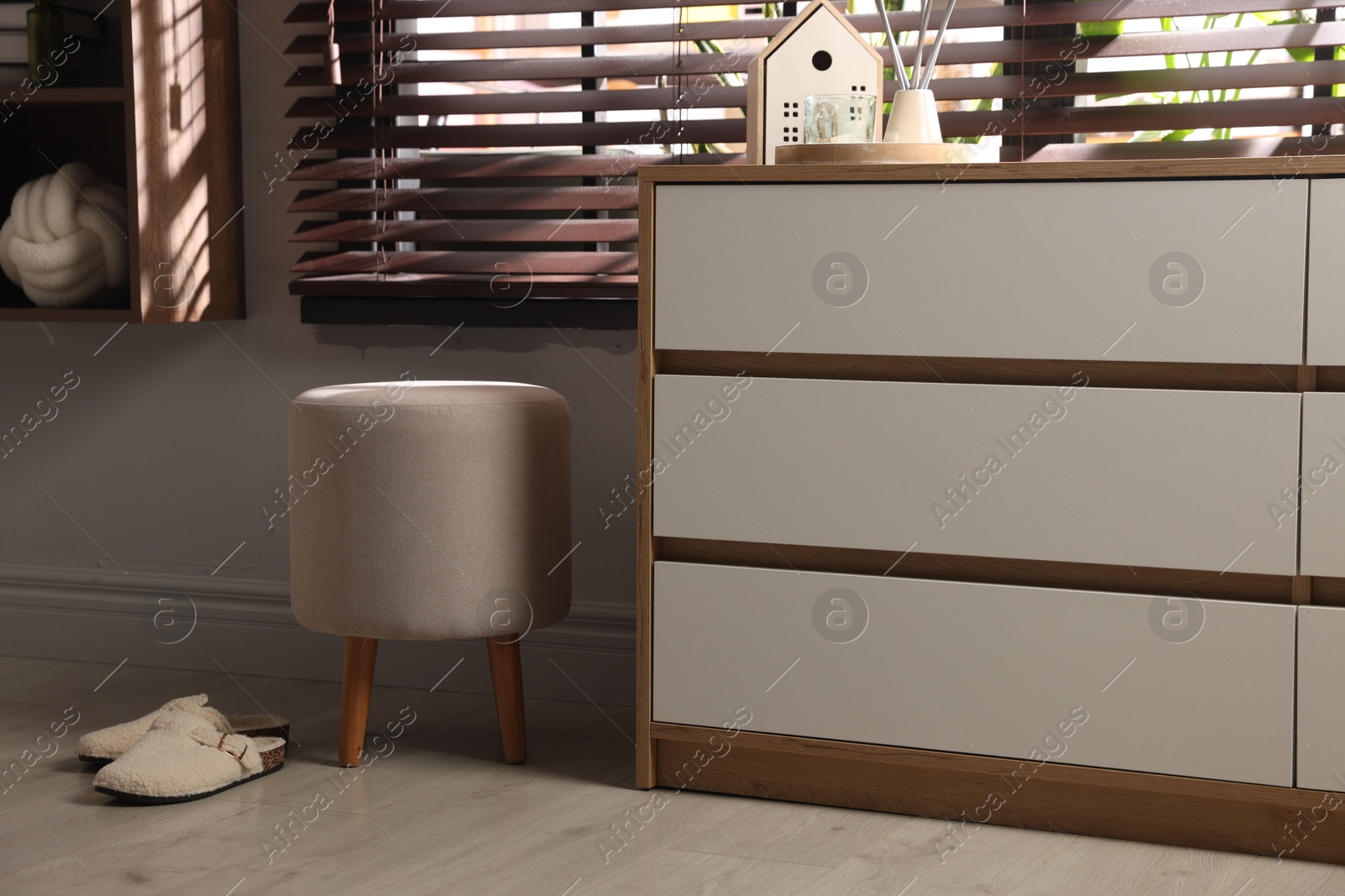 Stylish pouf and slippers near chest of drawers at home Photo of Stylish pouf and slippers near chest of drawers at home