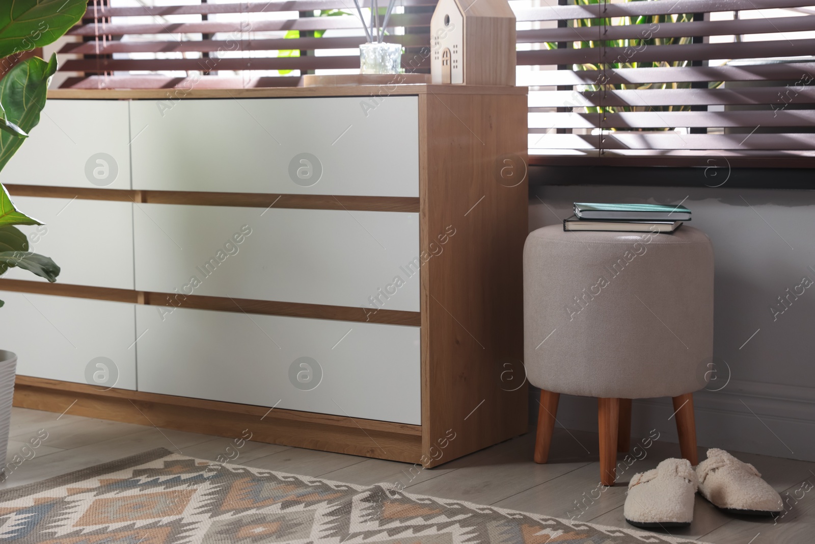 Stylish pouf with books and slippers near chest of drawers at home Photo of Stylish pouf with books and slippers near chest of drawers at home