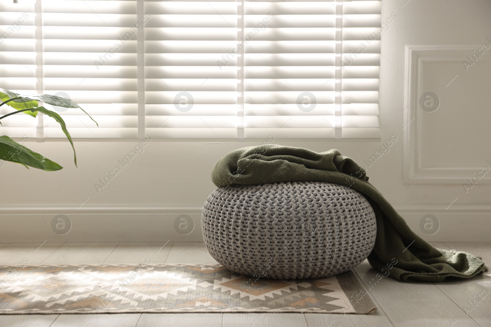 Stylish knitted pouf with plaid at home. Space for text Photo of Stylish knitted pouf with plaid at home. Space for text