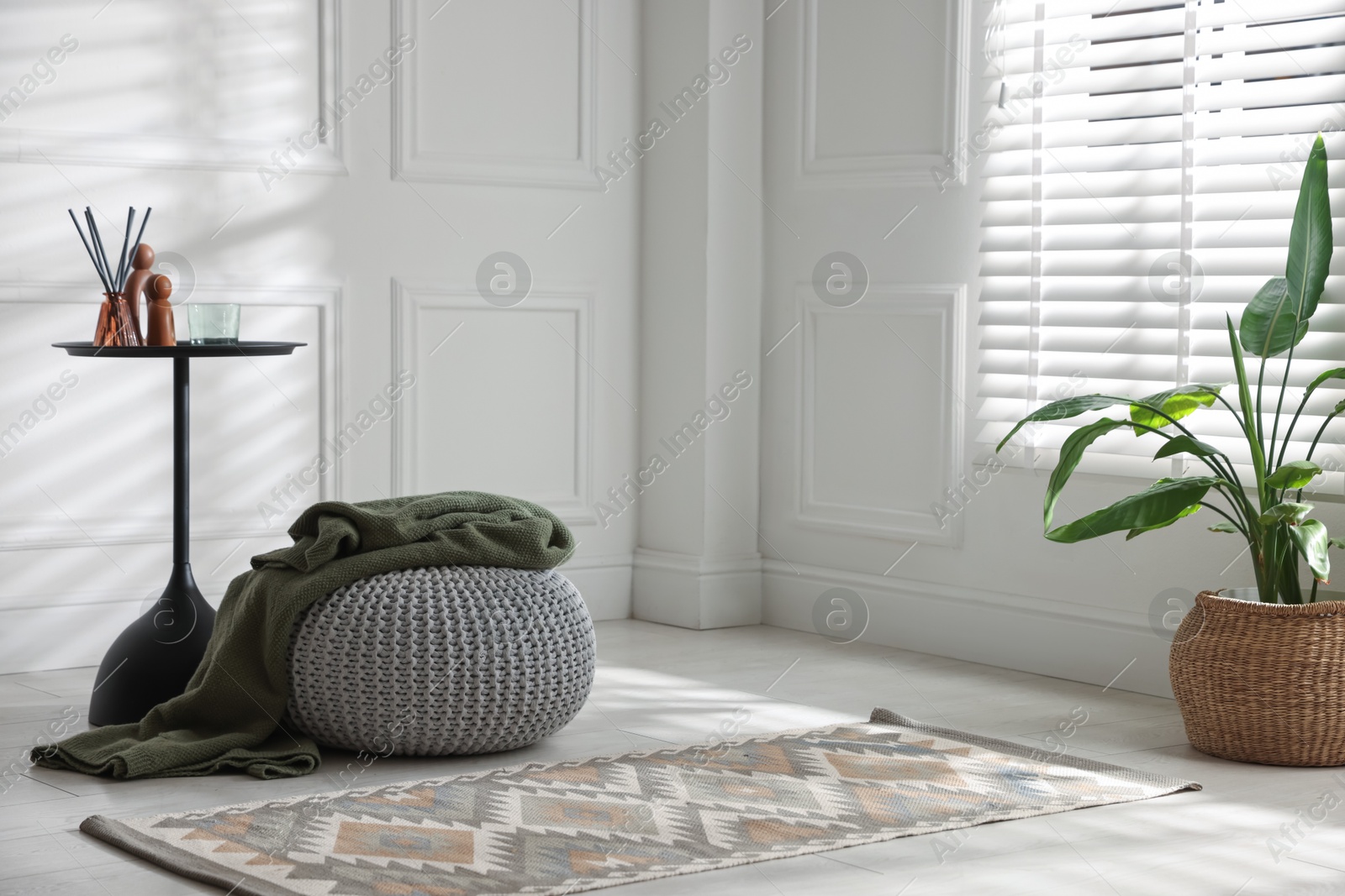 Stylish knitted pouf with plaid and home decor indoors. Space for text Photo of Stylish knitted pouf with plaid and home decor indoors. Space for text