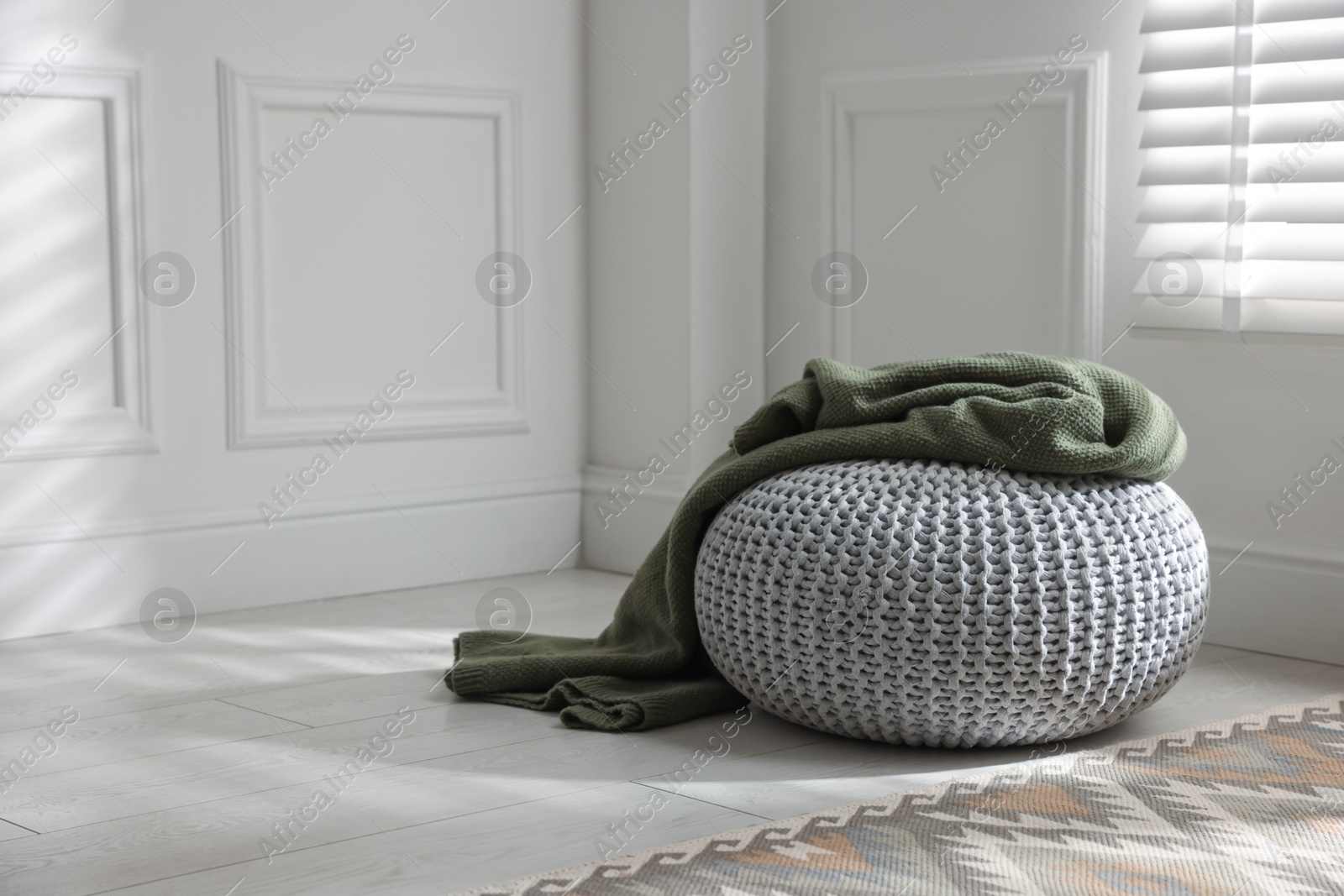 Stylish knitted pouf with plaid at home. Space for text Photo of Stylish knitted pouf with plaid at home. Space for text