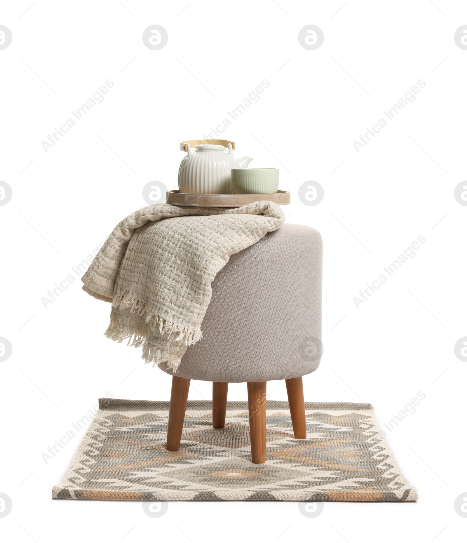Stylish pouf with tea set, plaid and rug isolated on white Photo of Stylish pouf with tea set, plaid and rug isolated on white