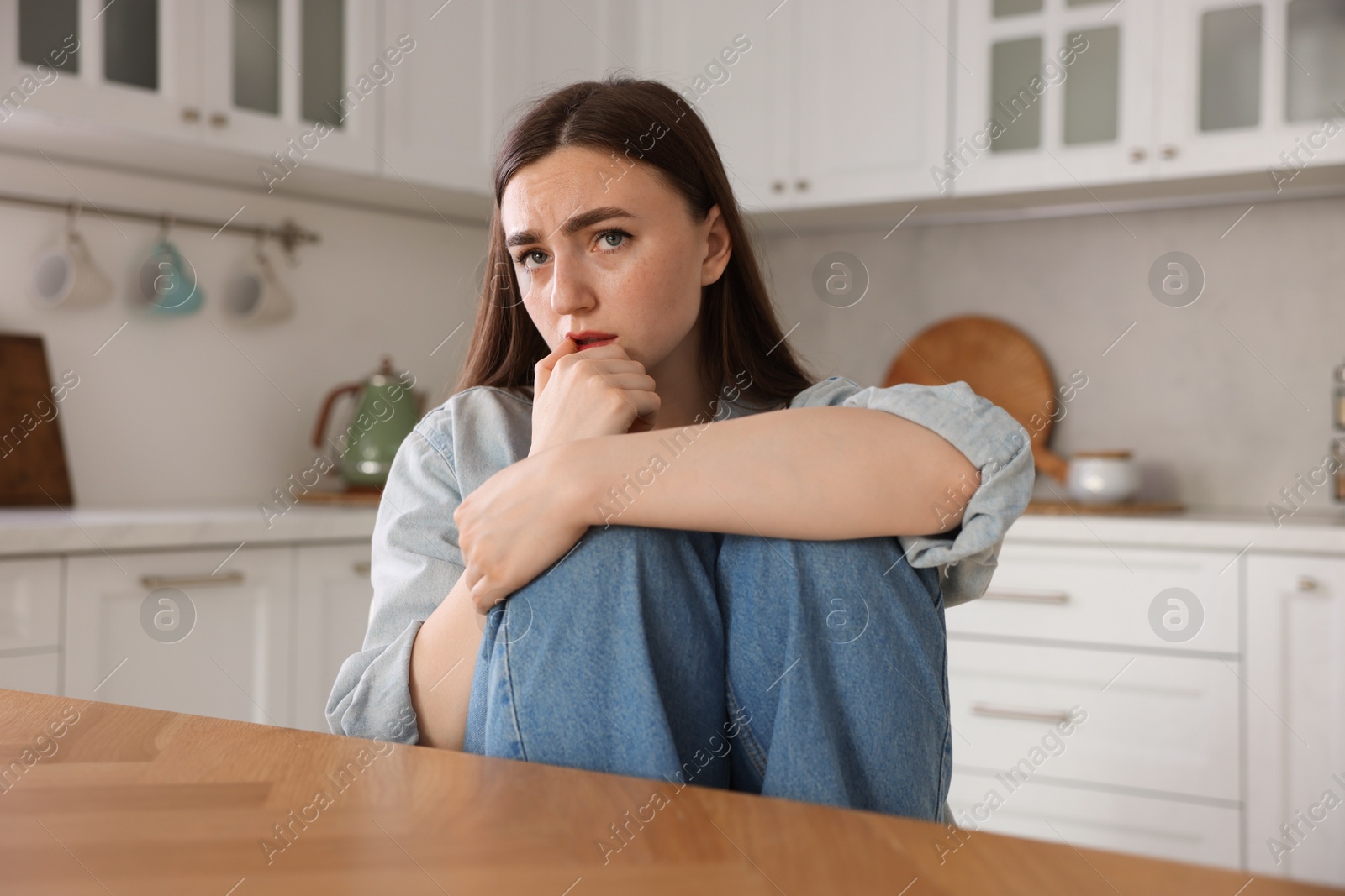 Worried woman suffering from paranoia at table in kitchen Photo of Worried woman suffering from paranoia at table in kitchen