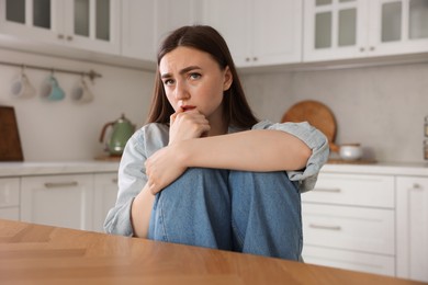 Photo of Worried woman suffering from paranoia at table in kitchen