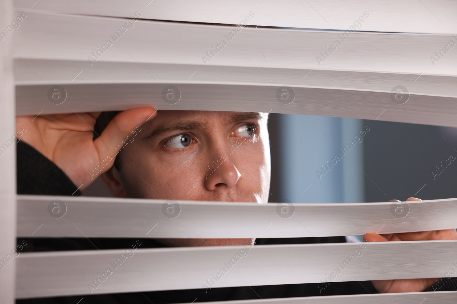 Paranoia. Worried man looking through window blinds indoors Photo of Paranoia. Worried man looking through window blinds indoors