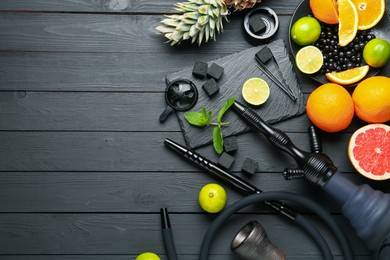 Photo of Hookah, coal and fresh fruits on black wooden table, flat lay. Space for text