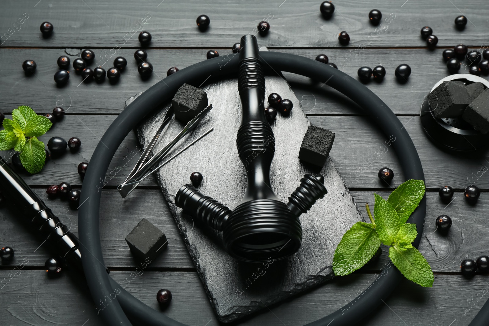 Photo of Hookah, coal, mint and currants on black wooden table, closeup