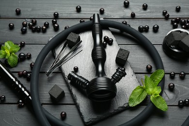 Photo of Hookah, coal, mint and currants on black wooden table, closeup