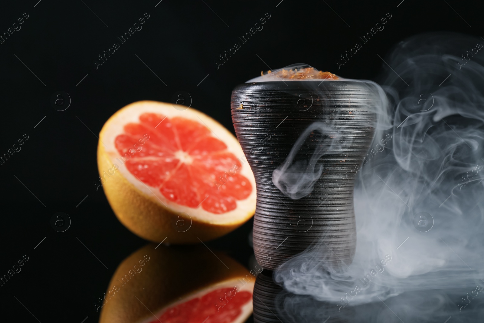 Photo of Hookah bowl with smoke and grapefruit on black table, closeup