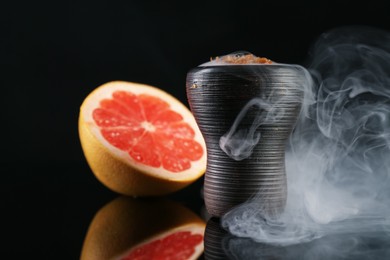 Photo of Hookah bowl with smoke and grapefruit on black table, closeup