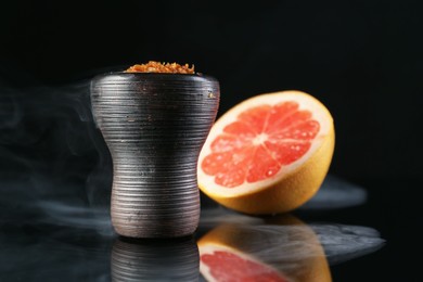 Photo of Hookah bowl with smoke and grapefruit on black table, closeup