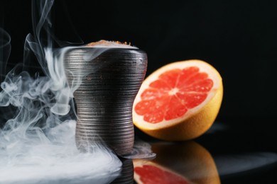 Photo of Hookah bowl with smoke and grapefruit on black table, closeup