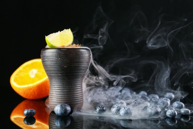 Photo of Hookah bowl with smoke and fruits on black table, closeup