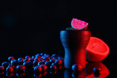 Photo of Hookah bowl with smoke and fruits on black table in neon lights, closeup. Space for text