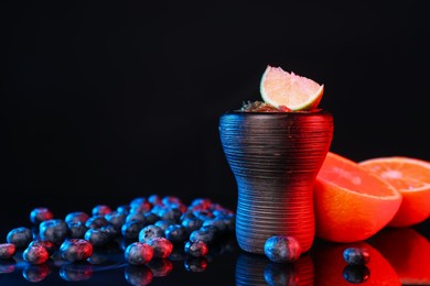 Photo of Hookah bowl with smoke and fruits on black table in neon lights, closeup. Space for text