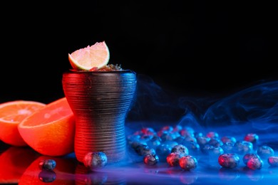 Photo of Hookah bowl with smoke and fruits on black table in neon lights, closeup. Space for text