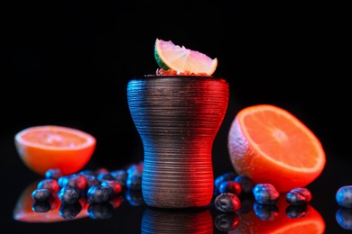 Photo of Hookah bowl with smoke and fruits on black table in neon lights, closeup