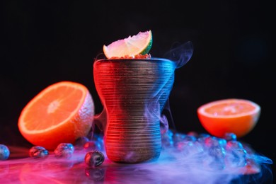 Photo of Hookah bowl with smoke and fruits on black table in neon lights, closeup