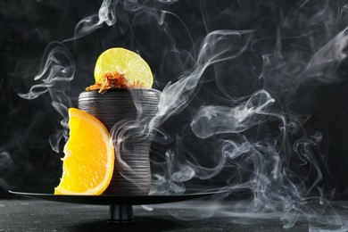 Photo of Hookah bowl with citrus fruits and smoke on black table, closeup