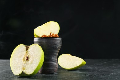Photo of Hookah bowl with apple pieces and smoke on black table, closeup. Space for text