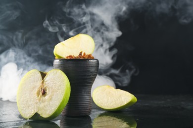 Photo of Hookah bowl with apple pieces and smoke on black table, closeup. Space for text