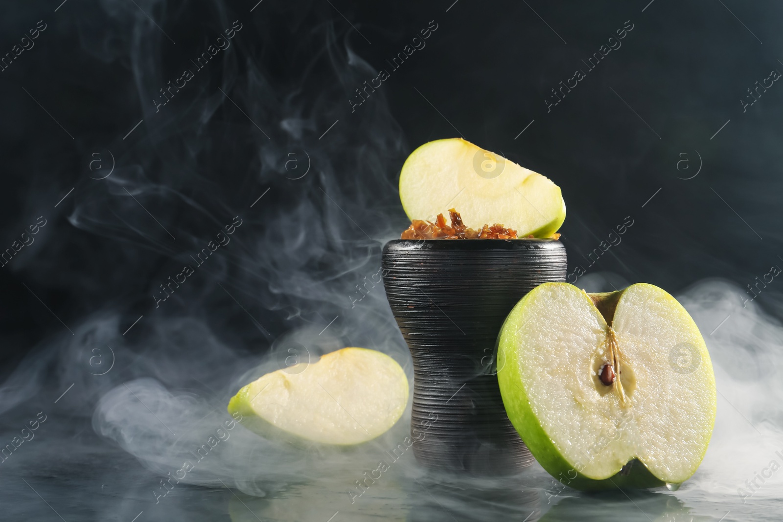 Photo of Hookah bowl with apple pieces and smoke on black table, closeup. Space for text