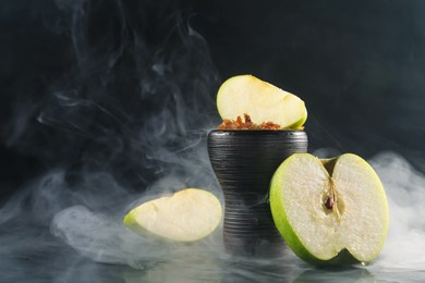 Photo of Hookah bowl with apple pieces and smoke on black table, closeup. Space for text