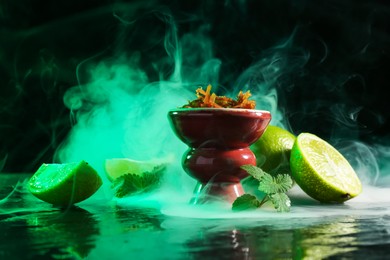Photo of Hookah bowl with limes, mint and smoke on black table, closeup