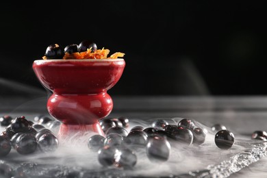 Photo of Hookah bowl with currants and smoke on black table, closeup. Space for text