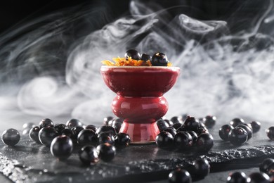 Photo of Hookah bowl with currants and smoke on black table, closeup