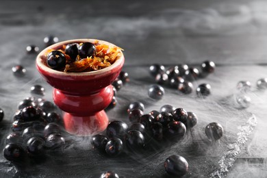 Photo of Hookah bowl with currants and smoke on black table, closeup