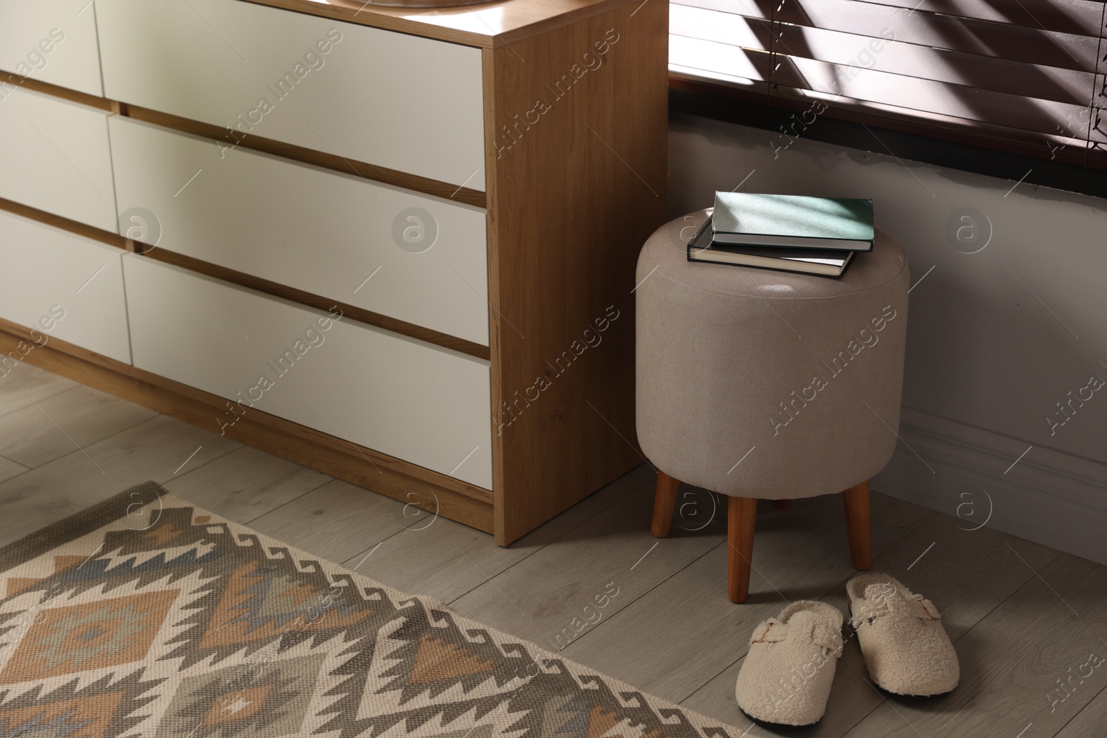 Stylish pouf with books and slippers near chest of drawers at home Photo of Stylish pouf with books and slippers near chest of drawers at home